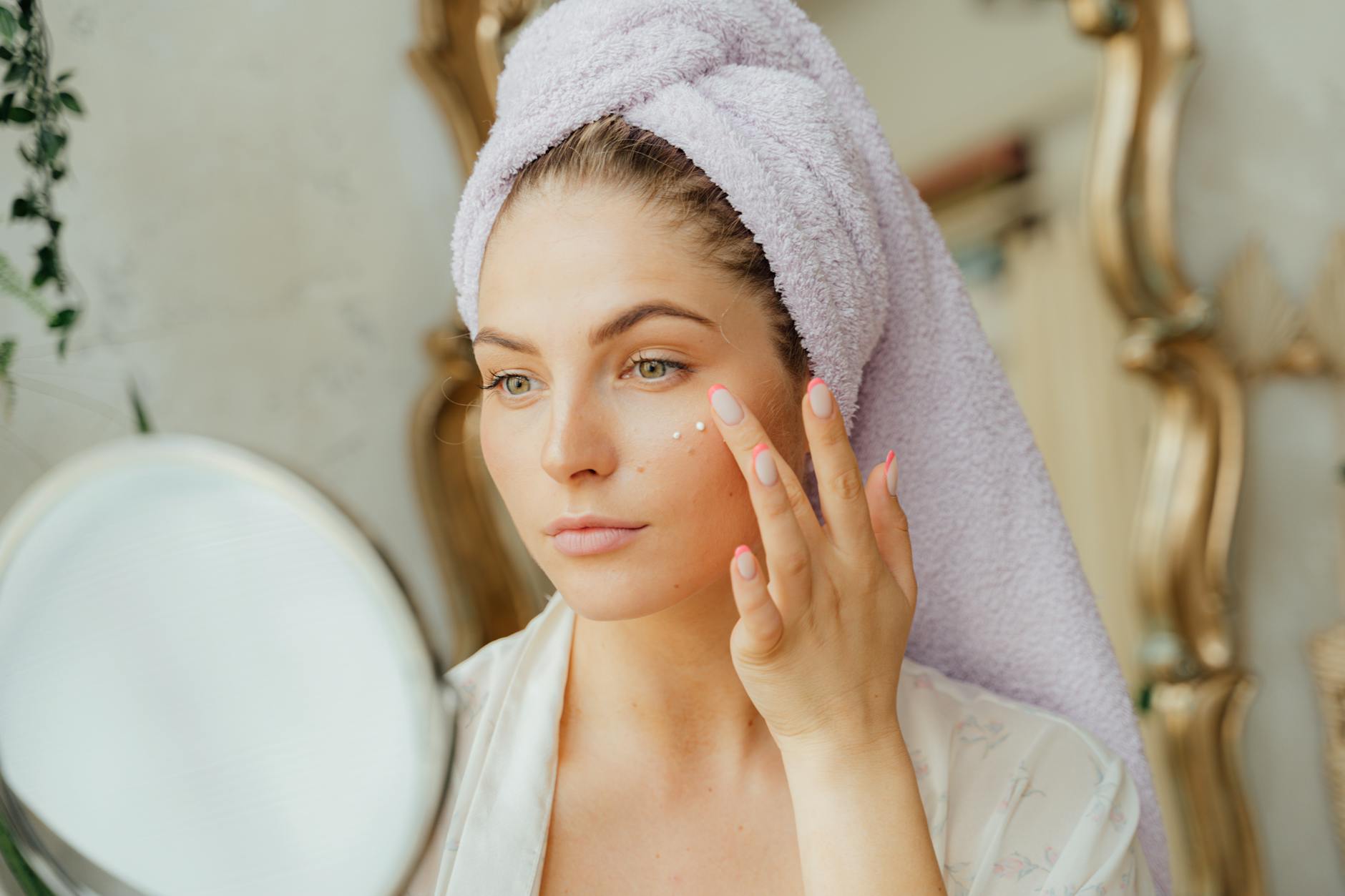 Kobieta z ręcznikiem na głowie nakłada naturalny krem przed lustrem